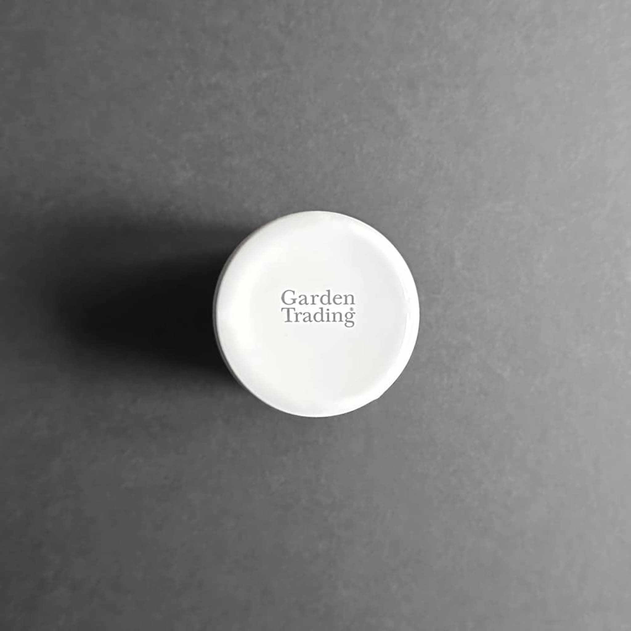 Base of a white cylindrical enamel toothbrush holder with 'Garden Trading' brand stamp on a grey background