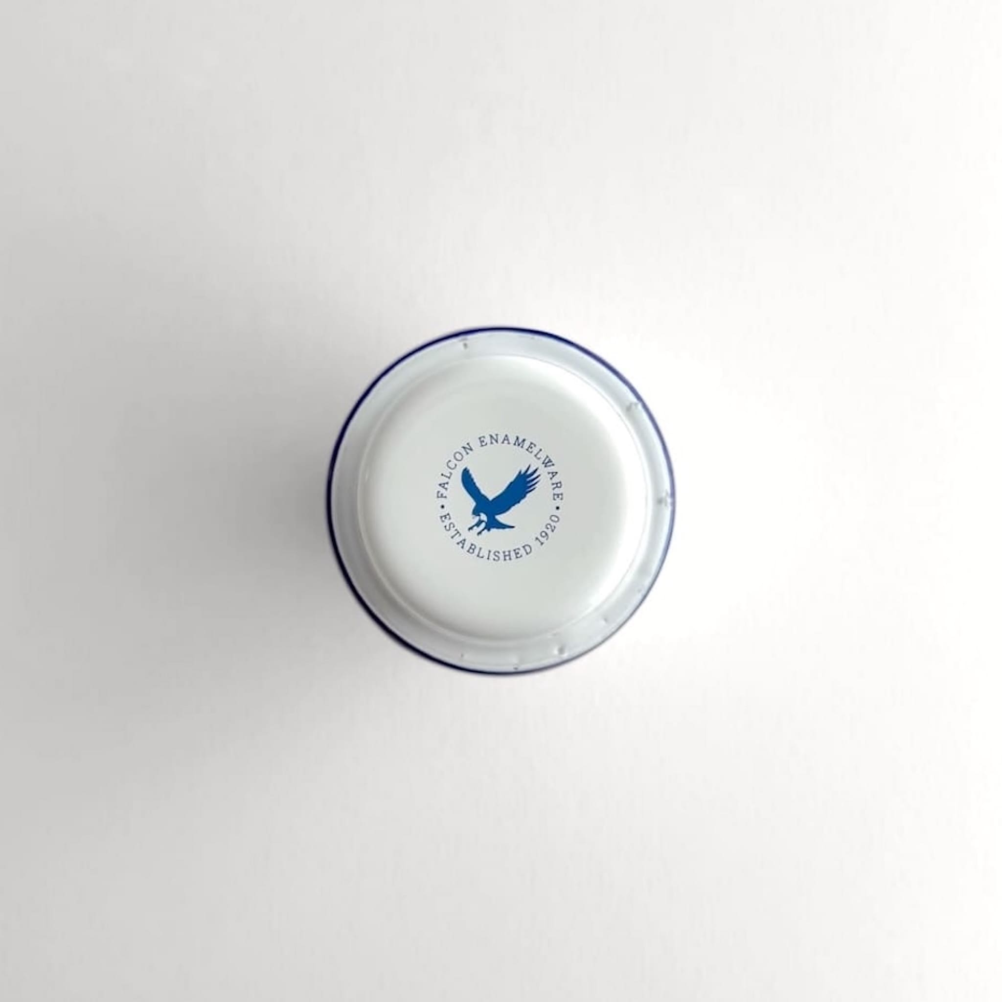 Underside view of a white Falcon enamelware tumbler with authenticity logo stamp