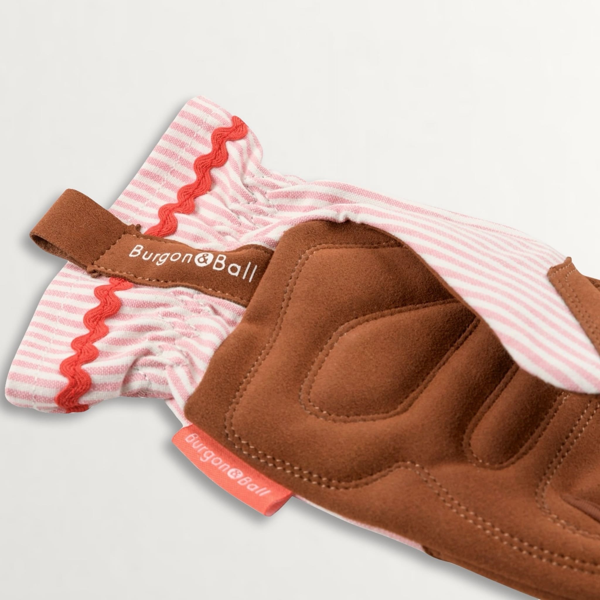 Close up showing quilted palms of gardening gloves in brown faux suede, pink striped backing and a ric rac trim to the wrist.