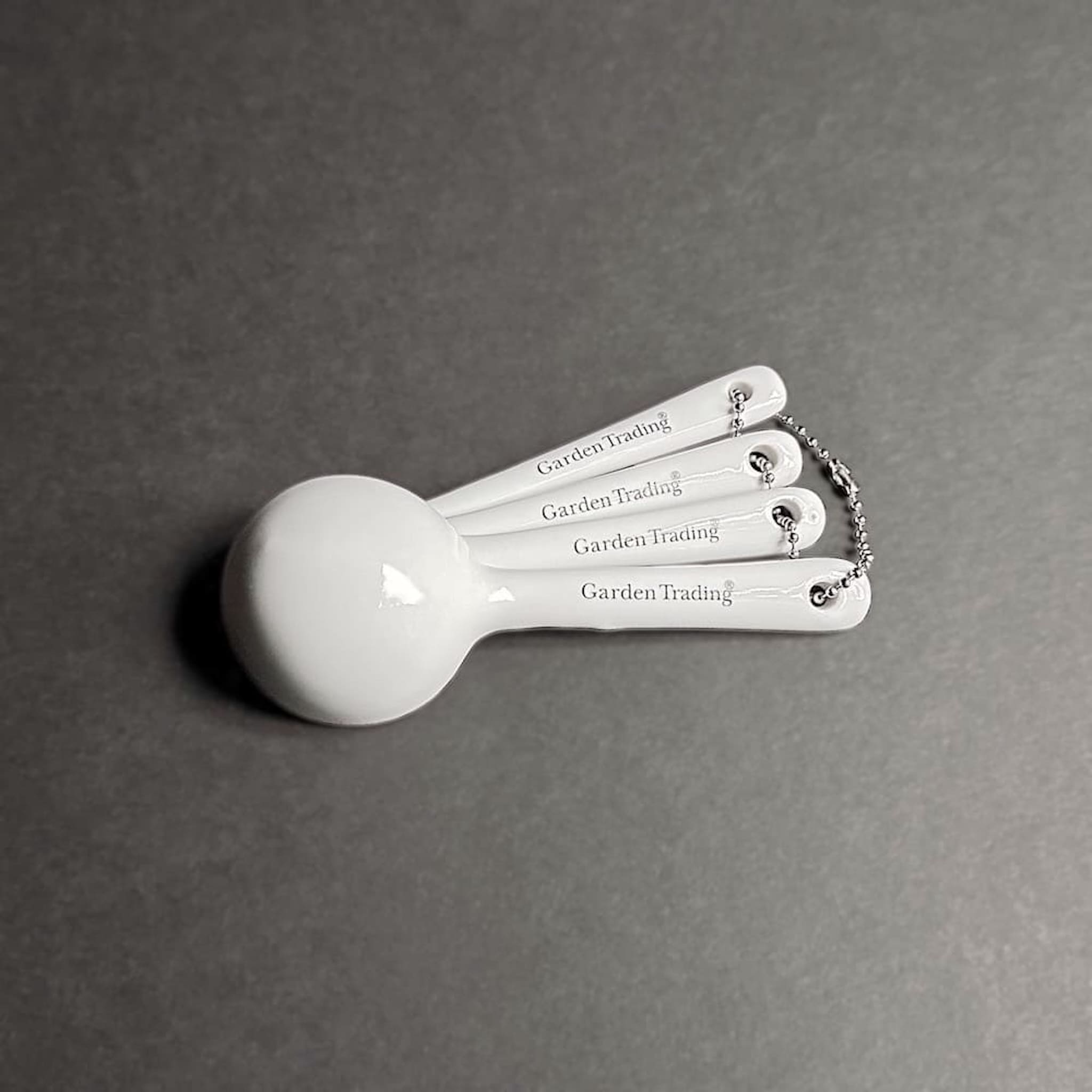 Set of white measuring spoons with 'Garden Trading' branding on a grey background