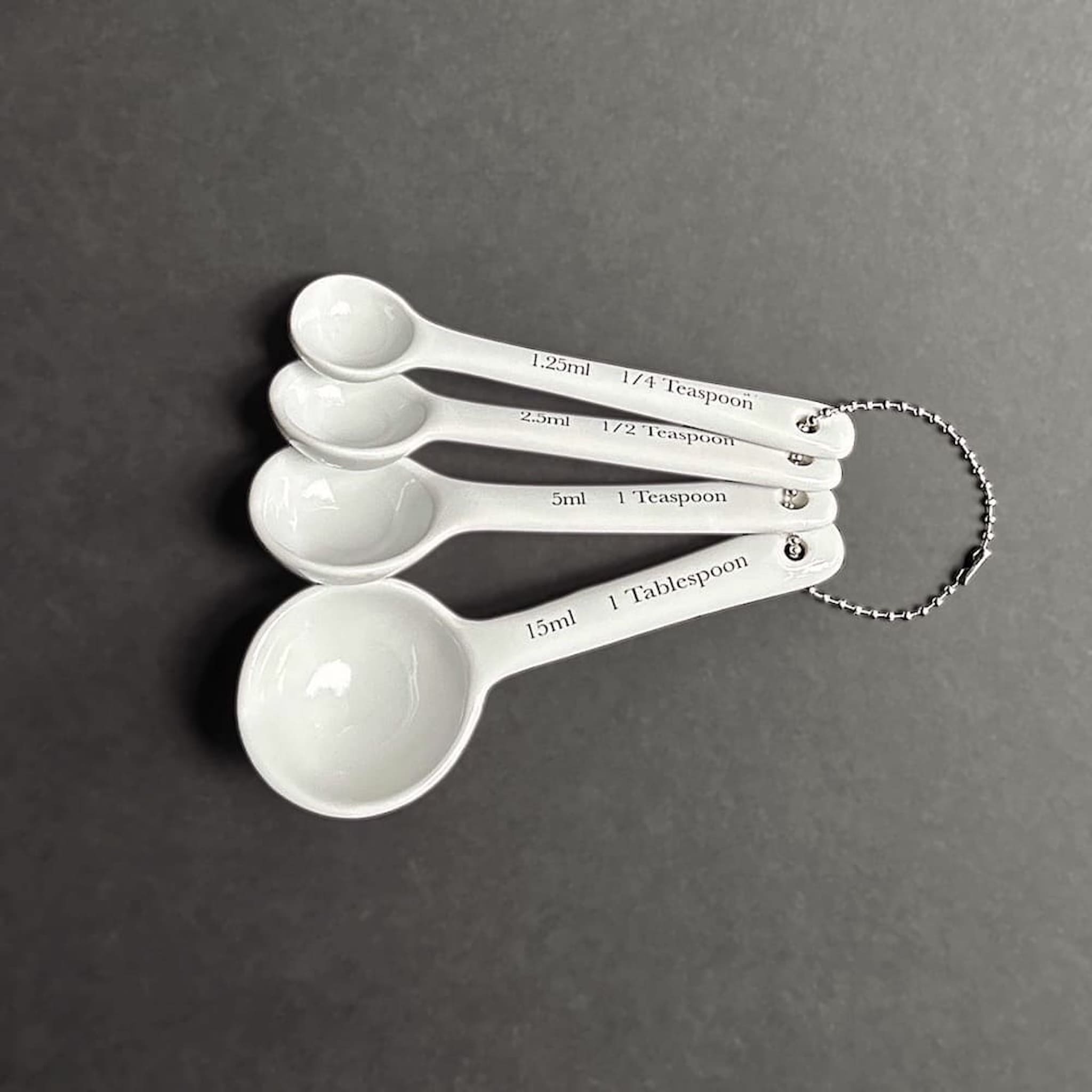 Set of four white ceramic measuring spoons with measurements on a grey background
