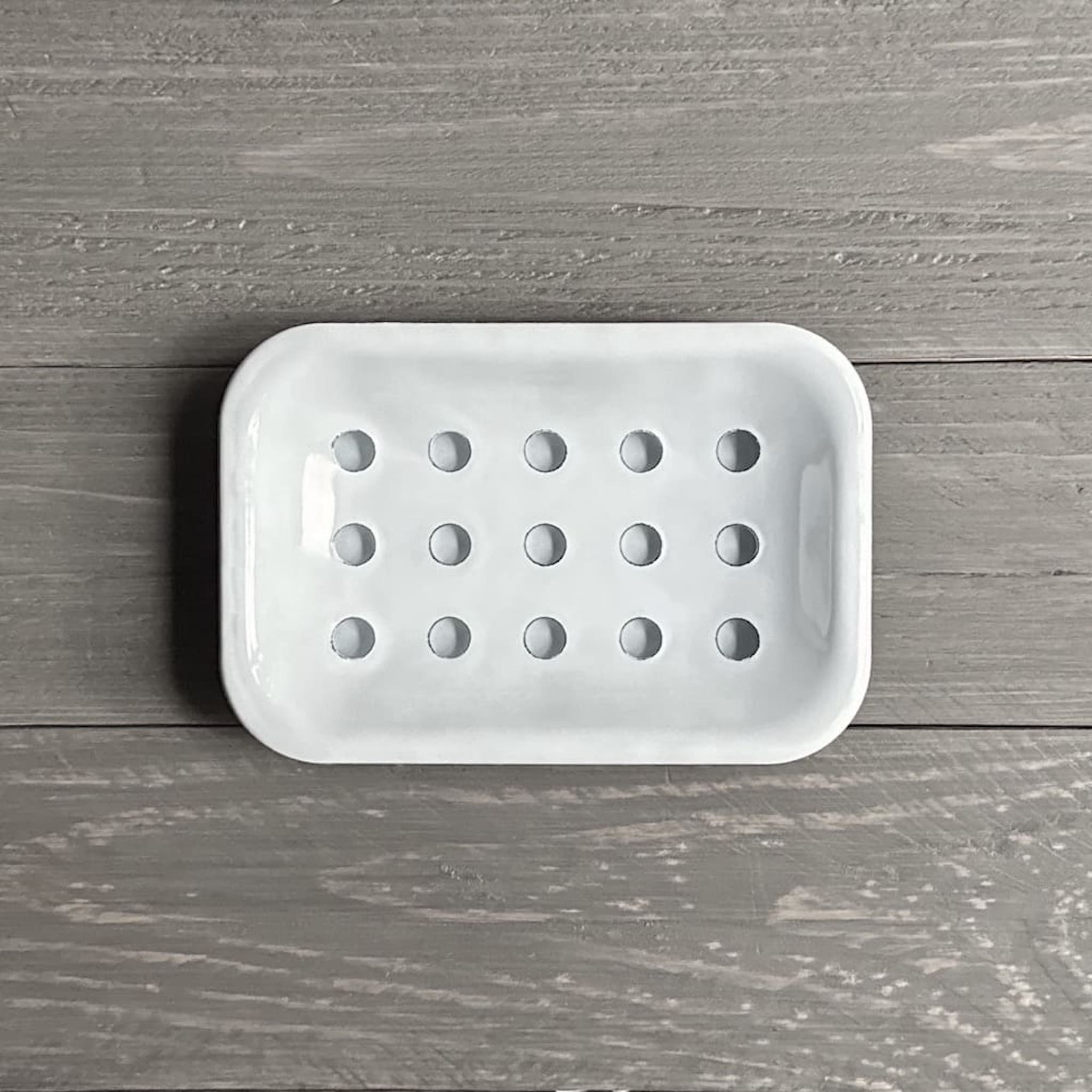 Above view of a white enamel soap dish with circular drainage holes on a wooden surface