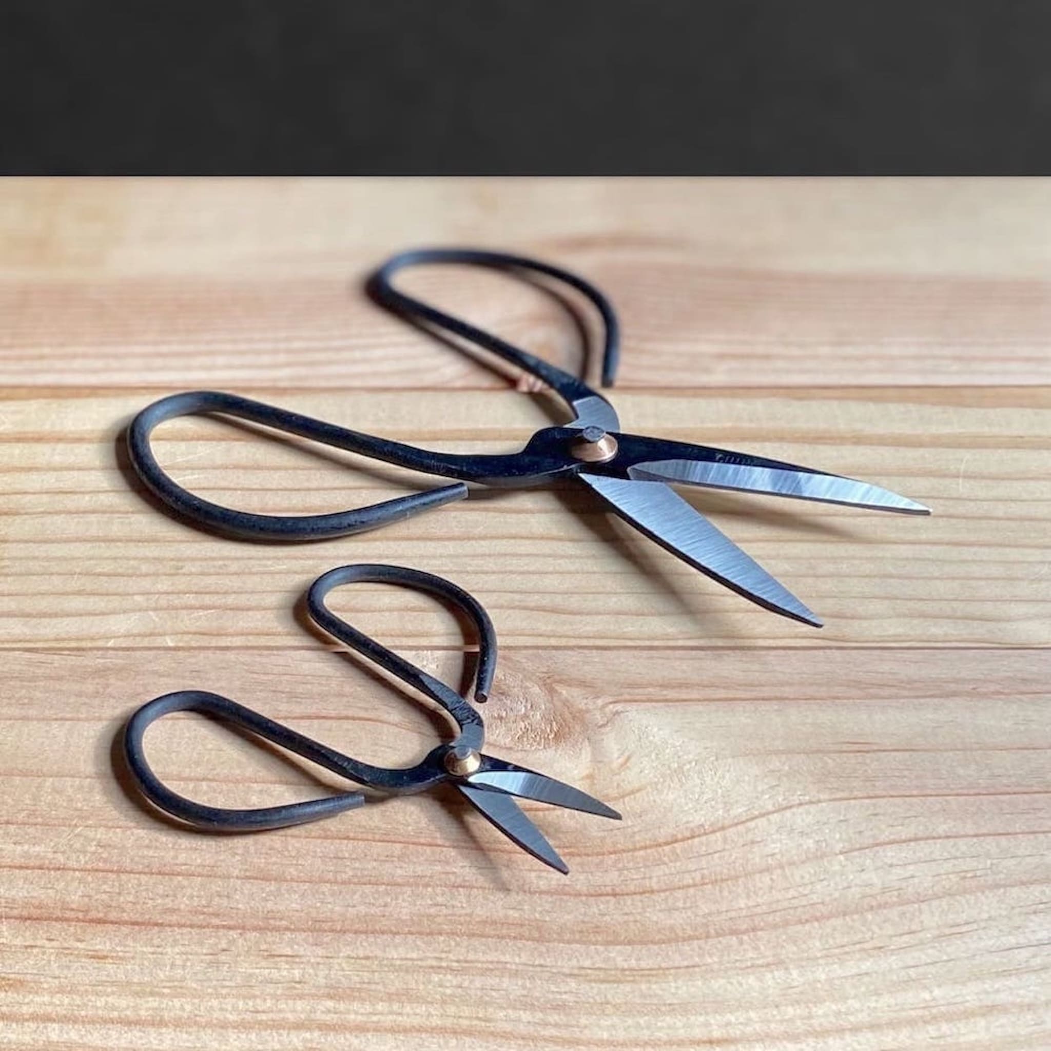 Two pairs of black-handled scissors on a wooden surface