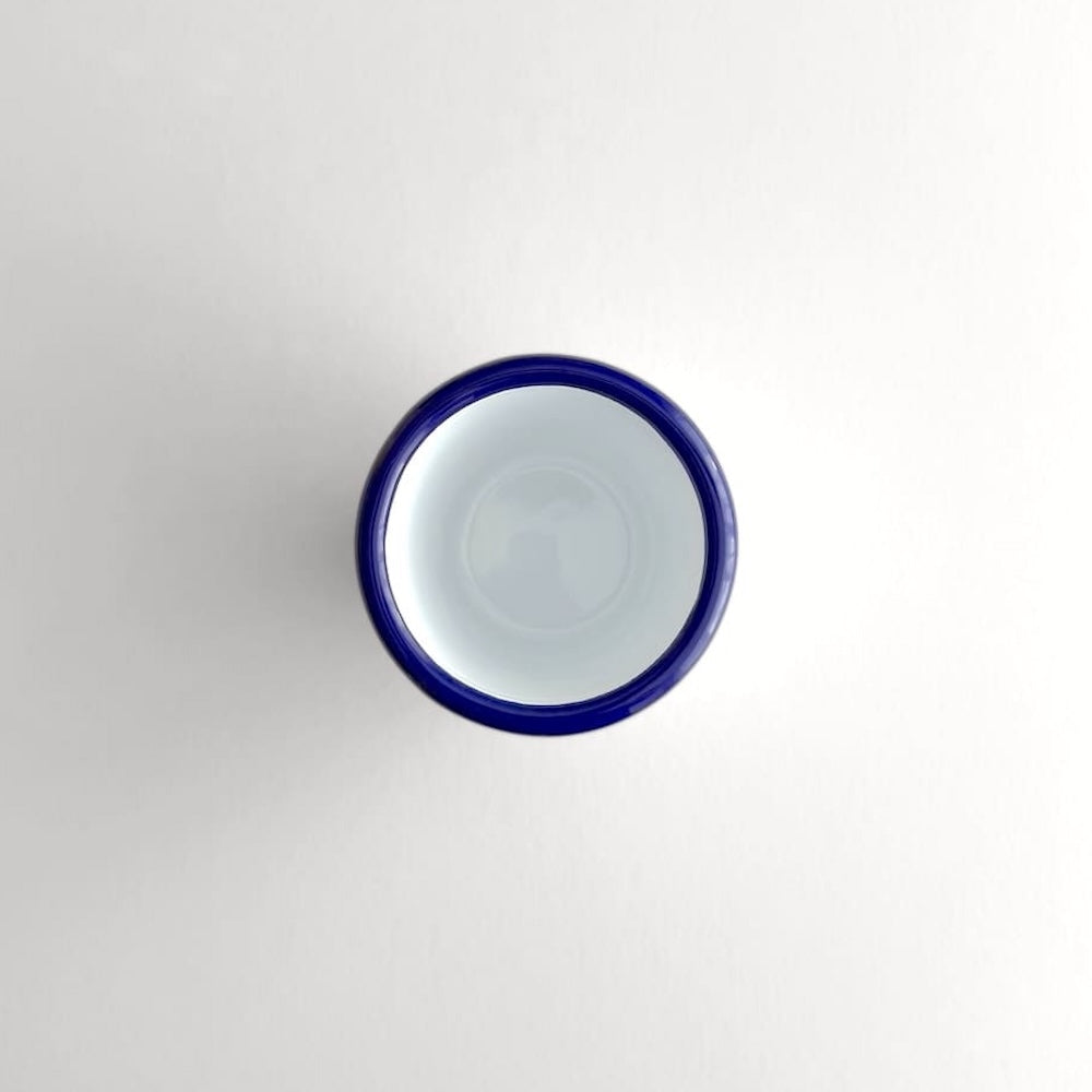 Above view of a white Falcon enamelware tumbler with a blue rim