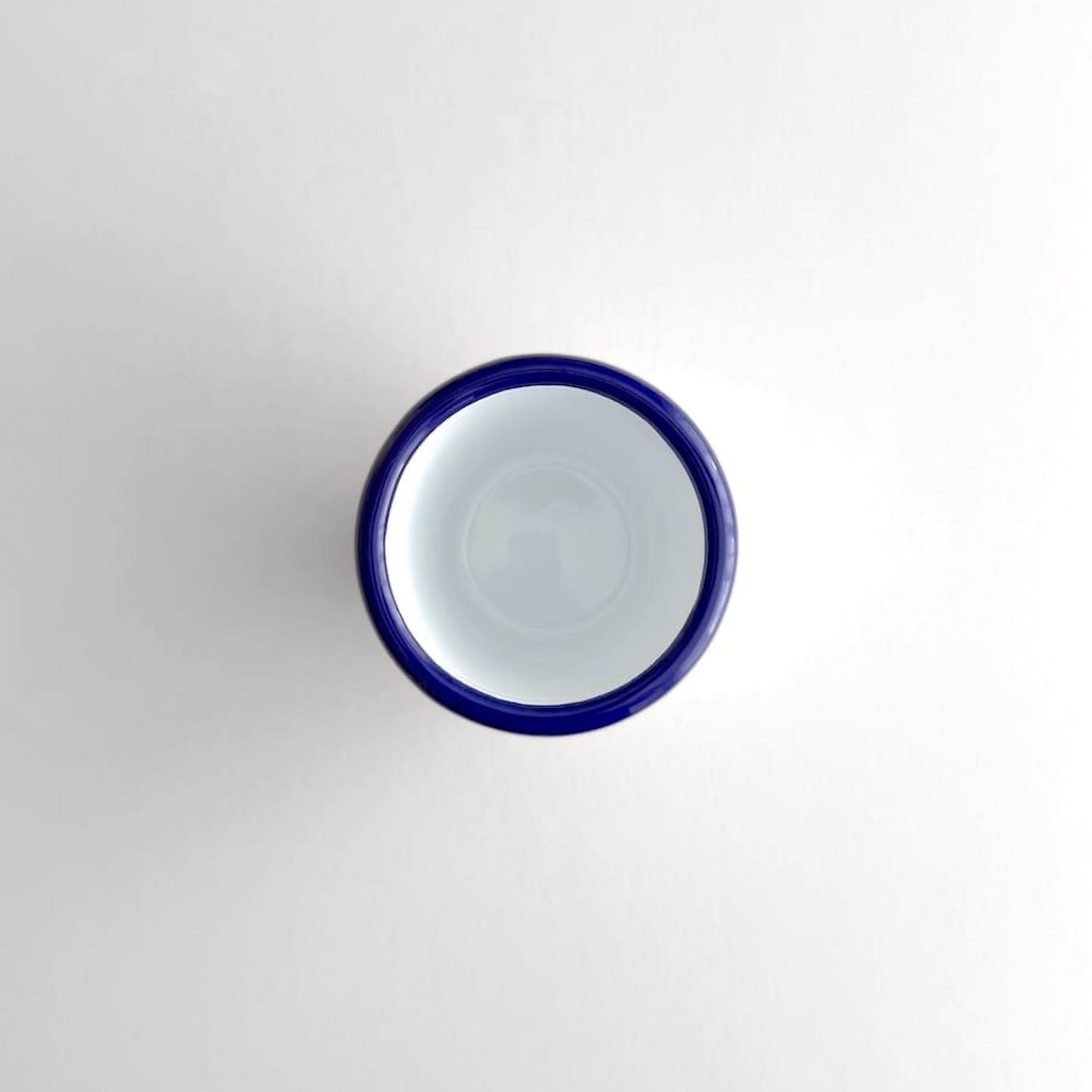 Above view of a white Falcon enamelware tumbler with a blue rim
