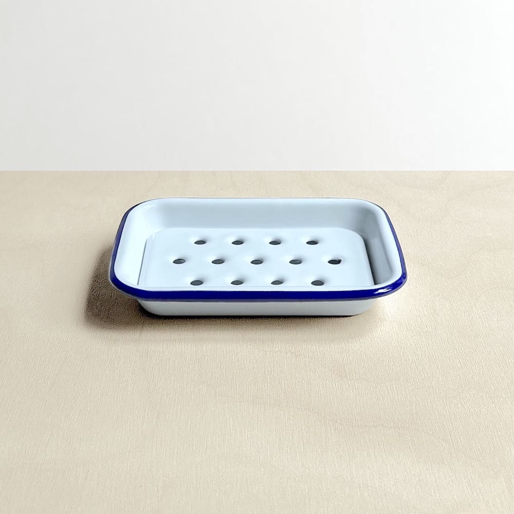 Side view of a white Falcon enamelware soap dish with blue rim