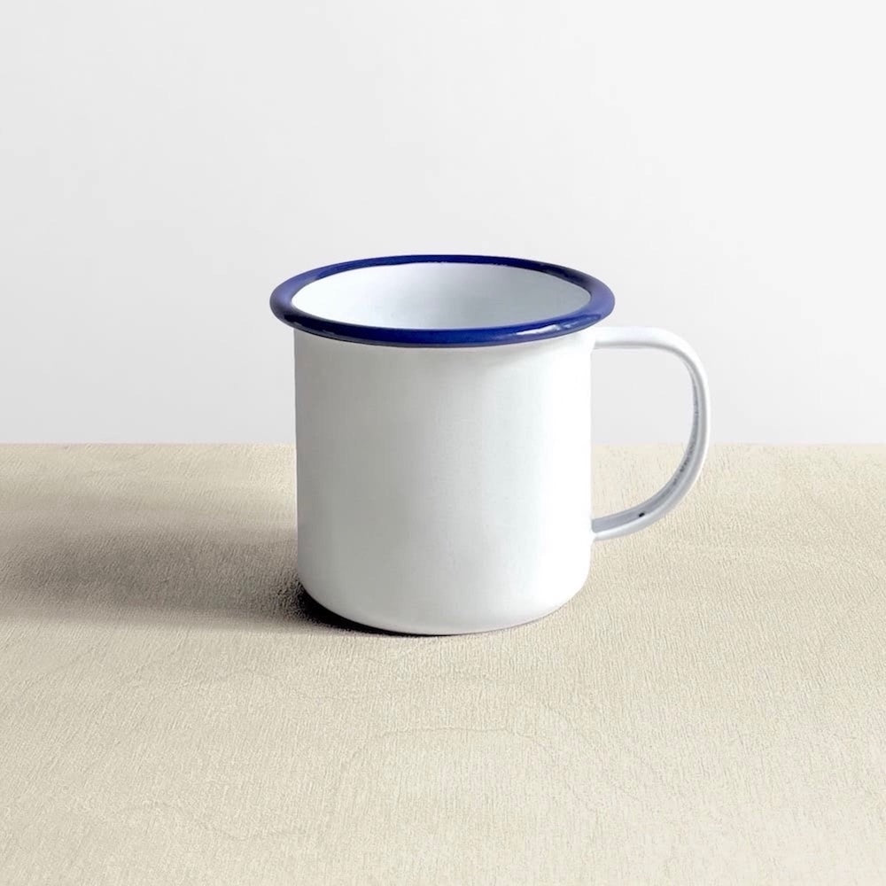 Side view of a white Falcon enamelware mug with blue rim 