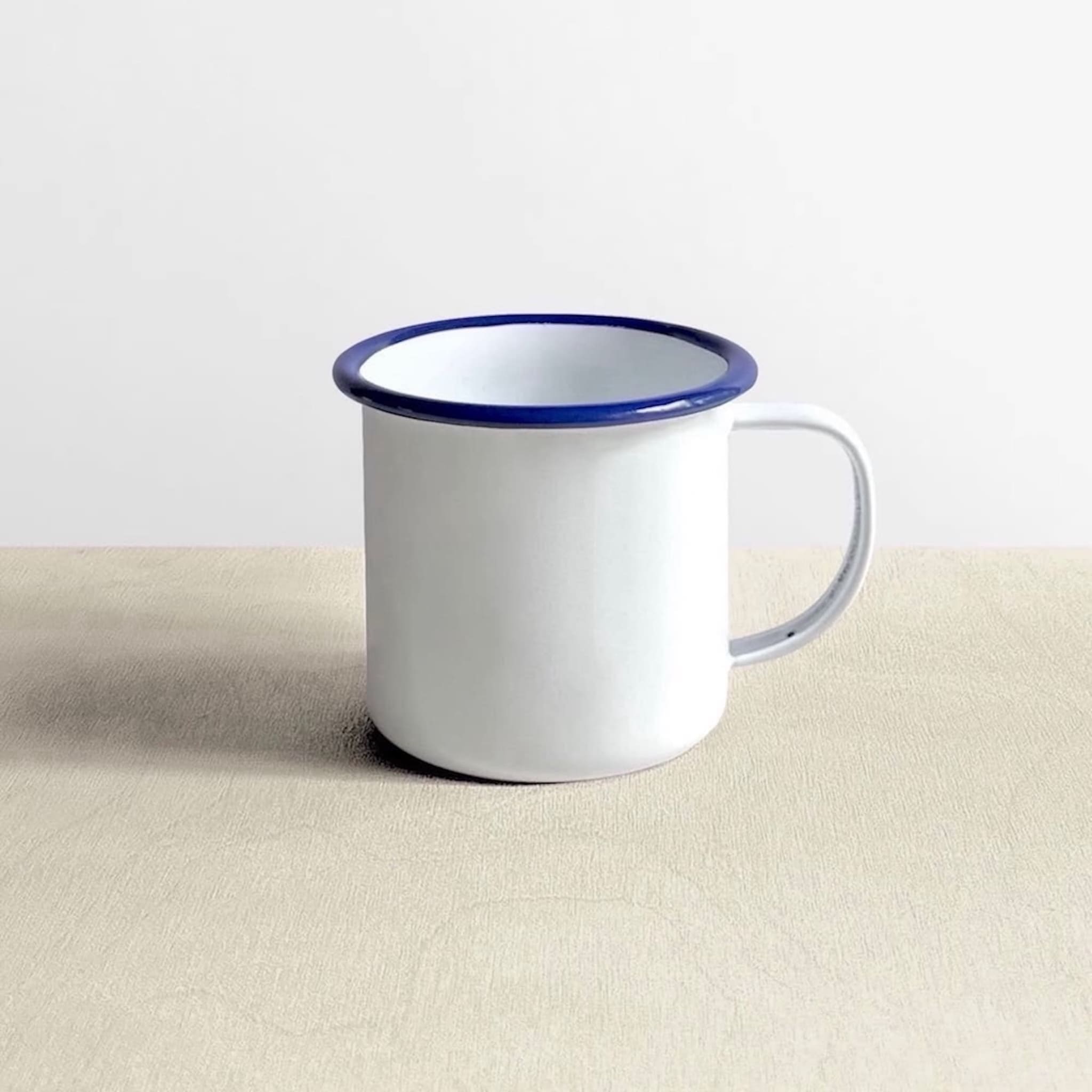 Side view of a white Falcon enamelware mug with blue rim 