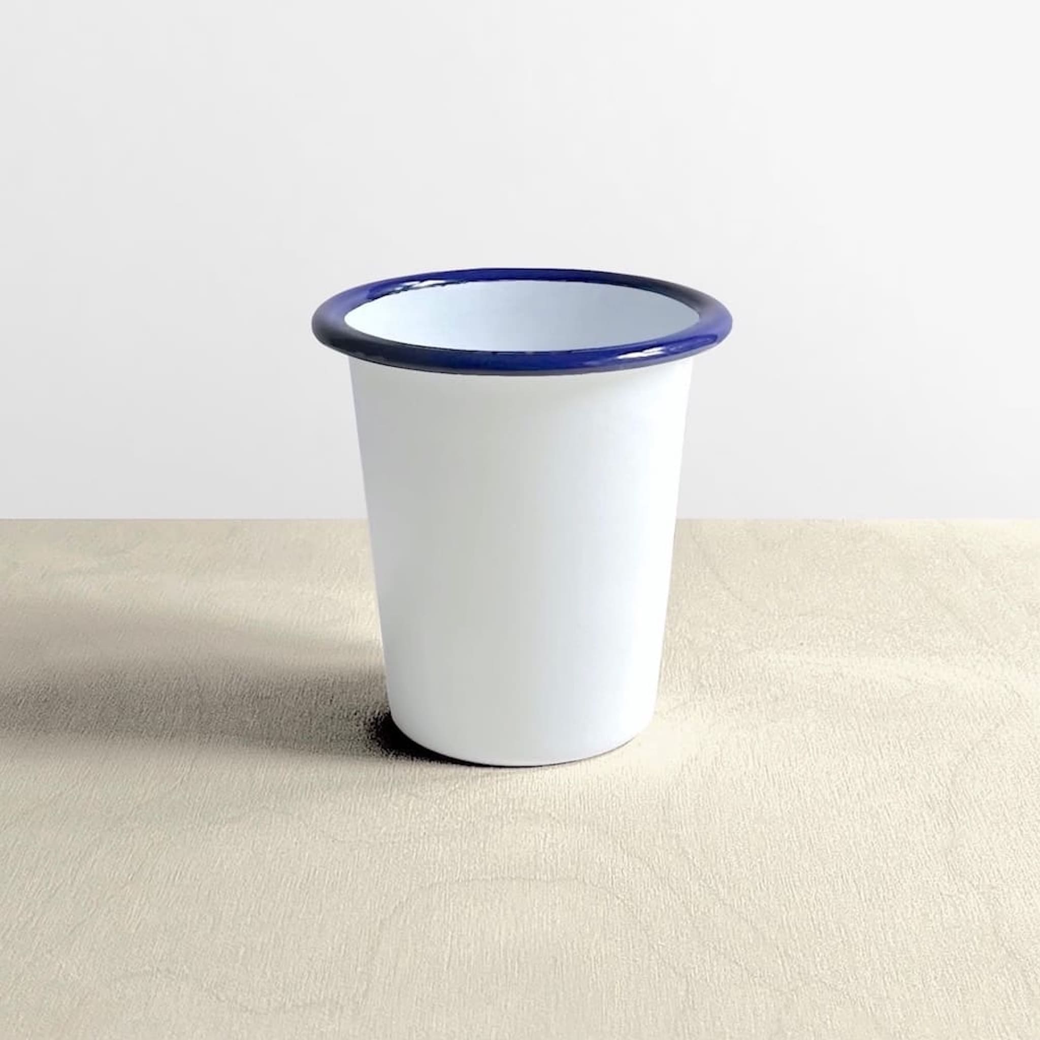 Side view of a white Falcon enamelware tumbler with blue rim 