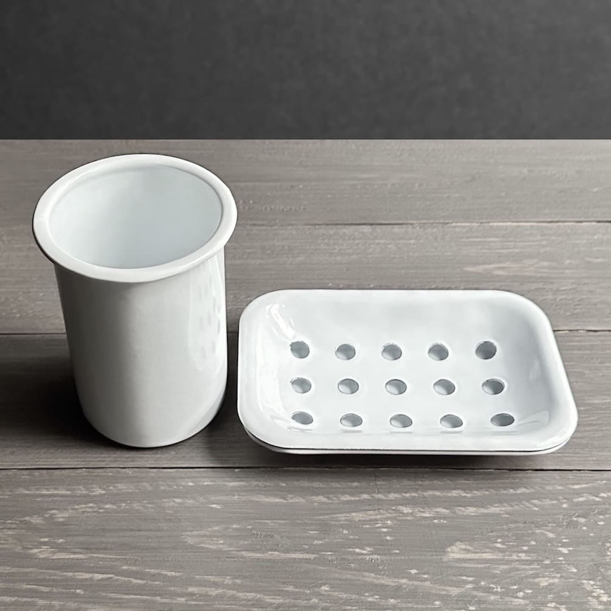 Side view of white enamel toothbrush holder and soap dish on a wooden surface