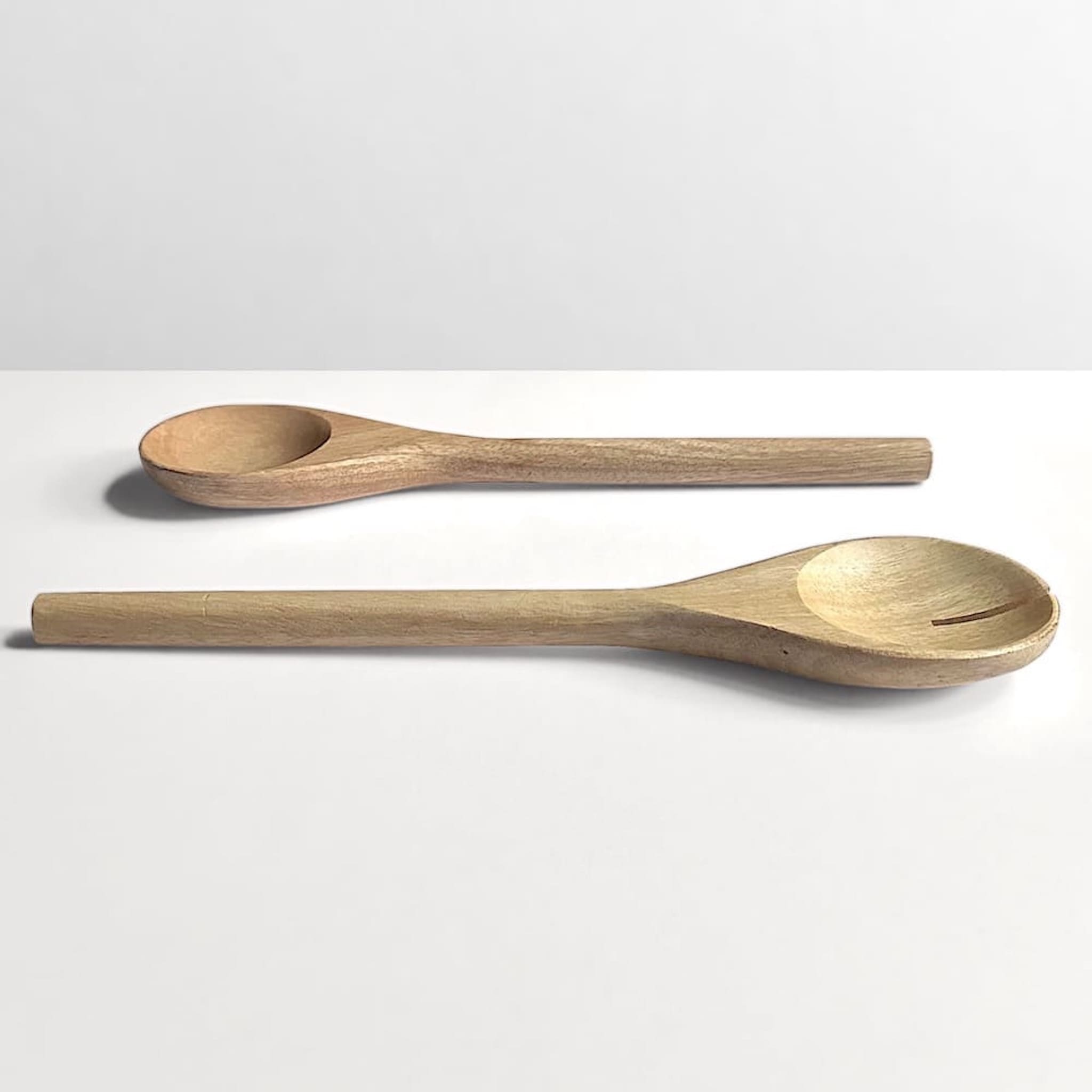 Side view of a pair of mango wood salad servers on an off-white background