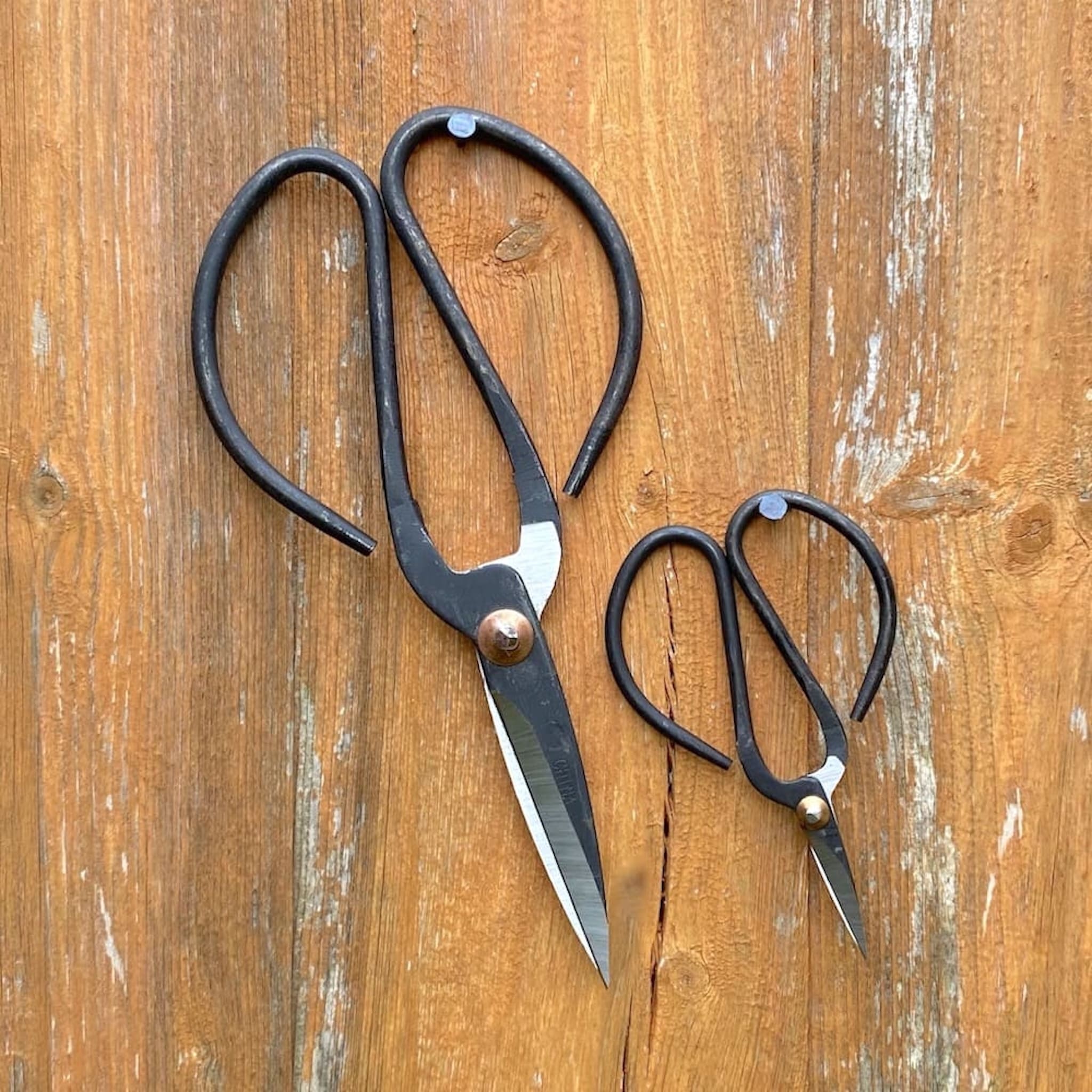 Two pairs of black-handled scissors hanging on a wooden surface