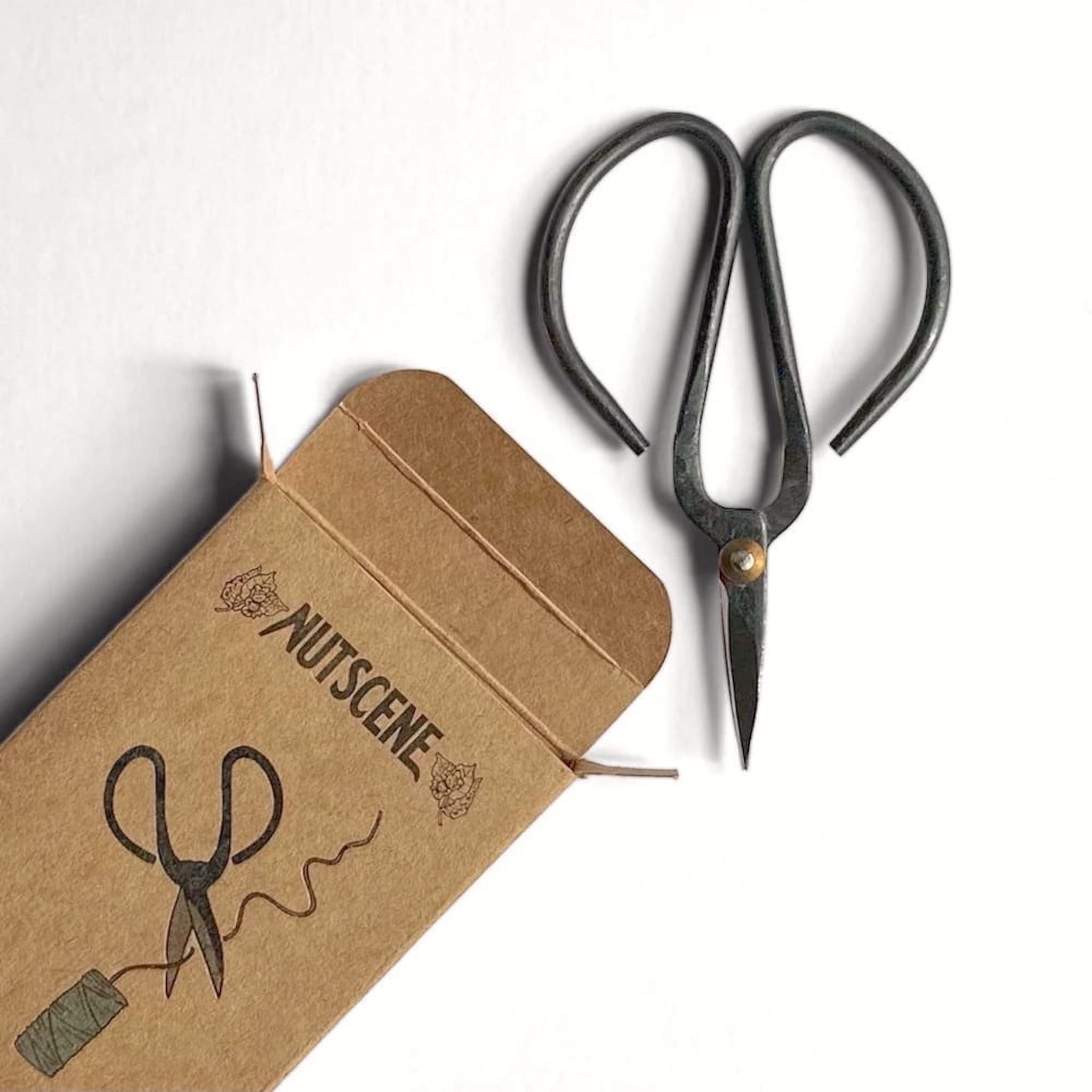 Pair of black-handled shears with a Nutscene branded brown box on a white background