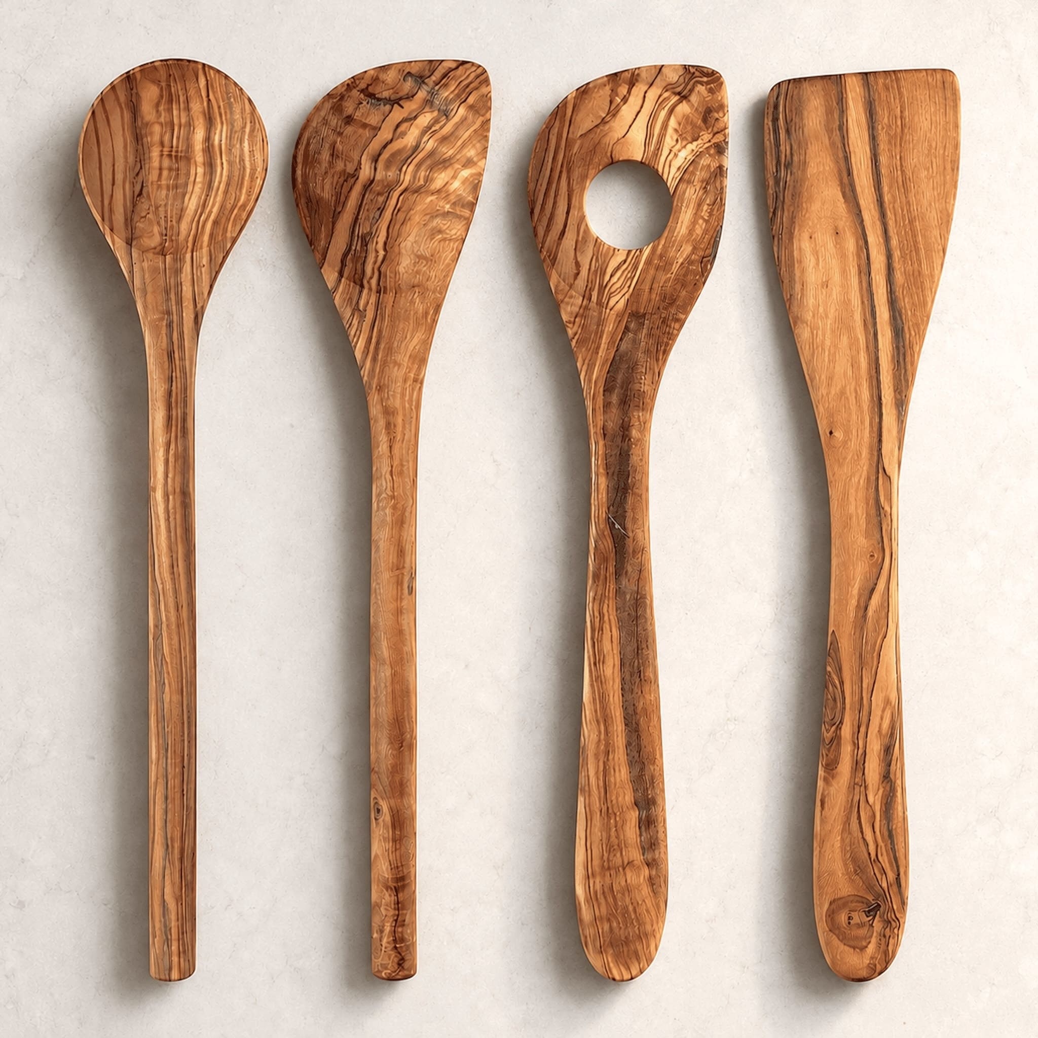 Four olive wood kitchen utensils with natural grain patterns, arranged vertically on a light textured background.