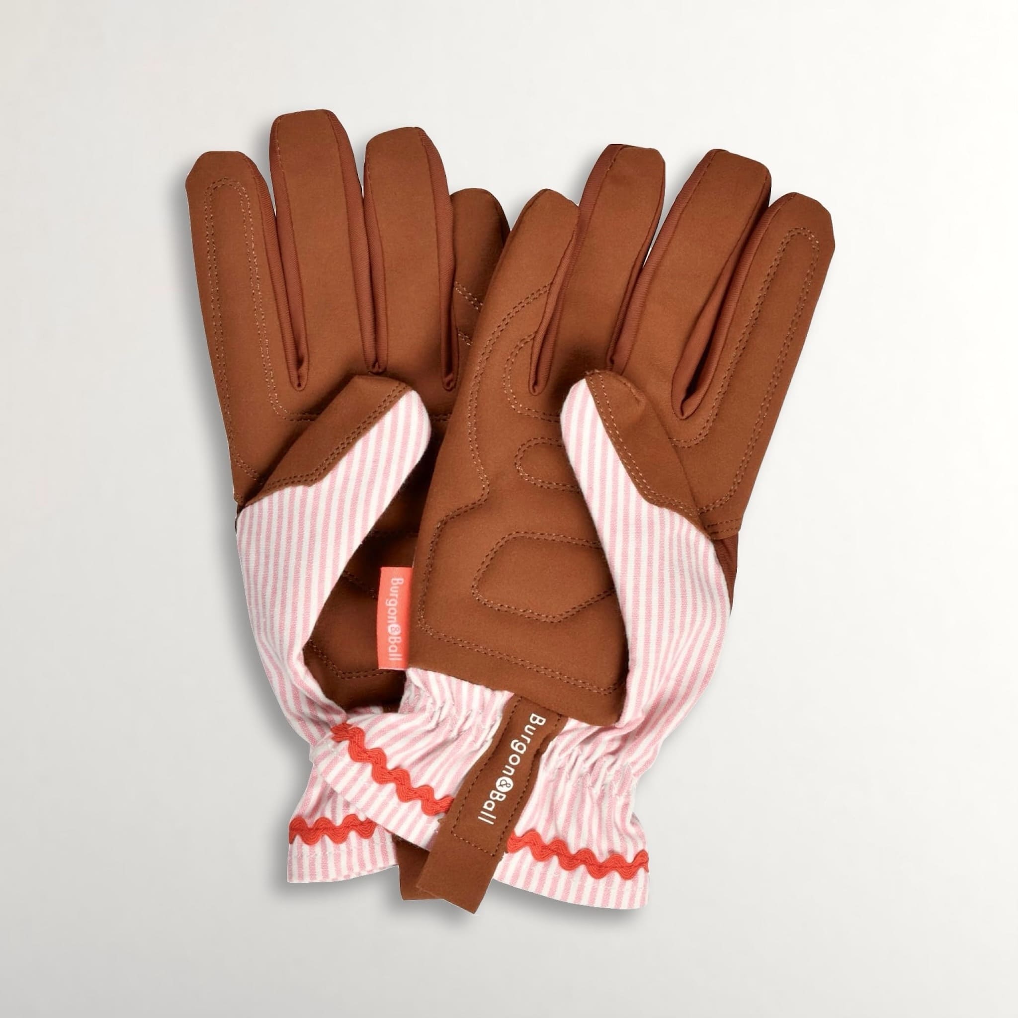 Brown gardening gloves with pink and white striped cotton backs on a light grey background.
