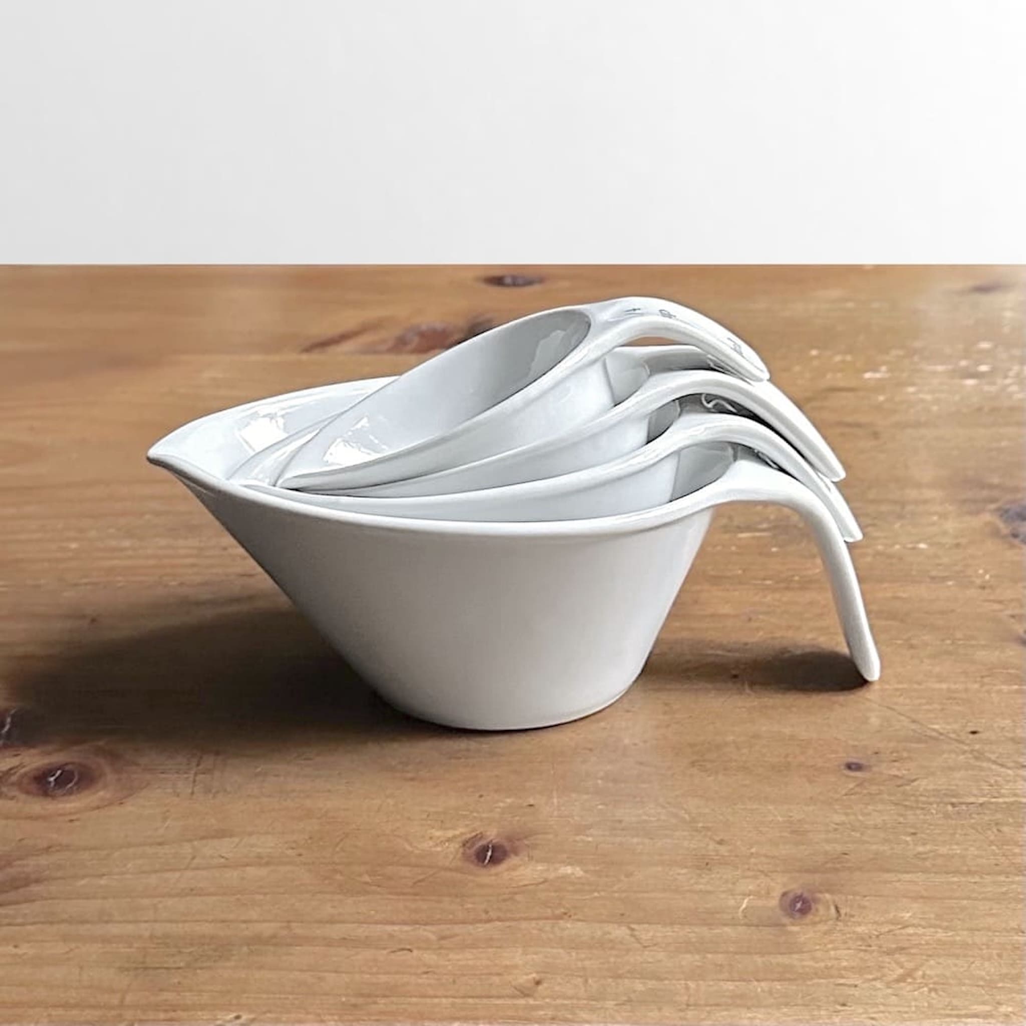 Side view of a set of four white ceramic measuring cups stacked on a wooden surface