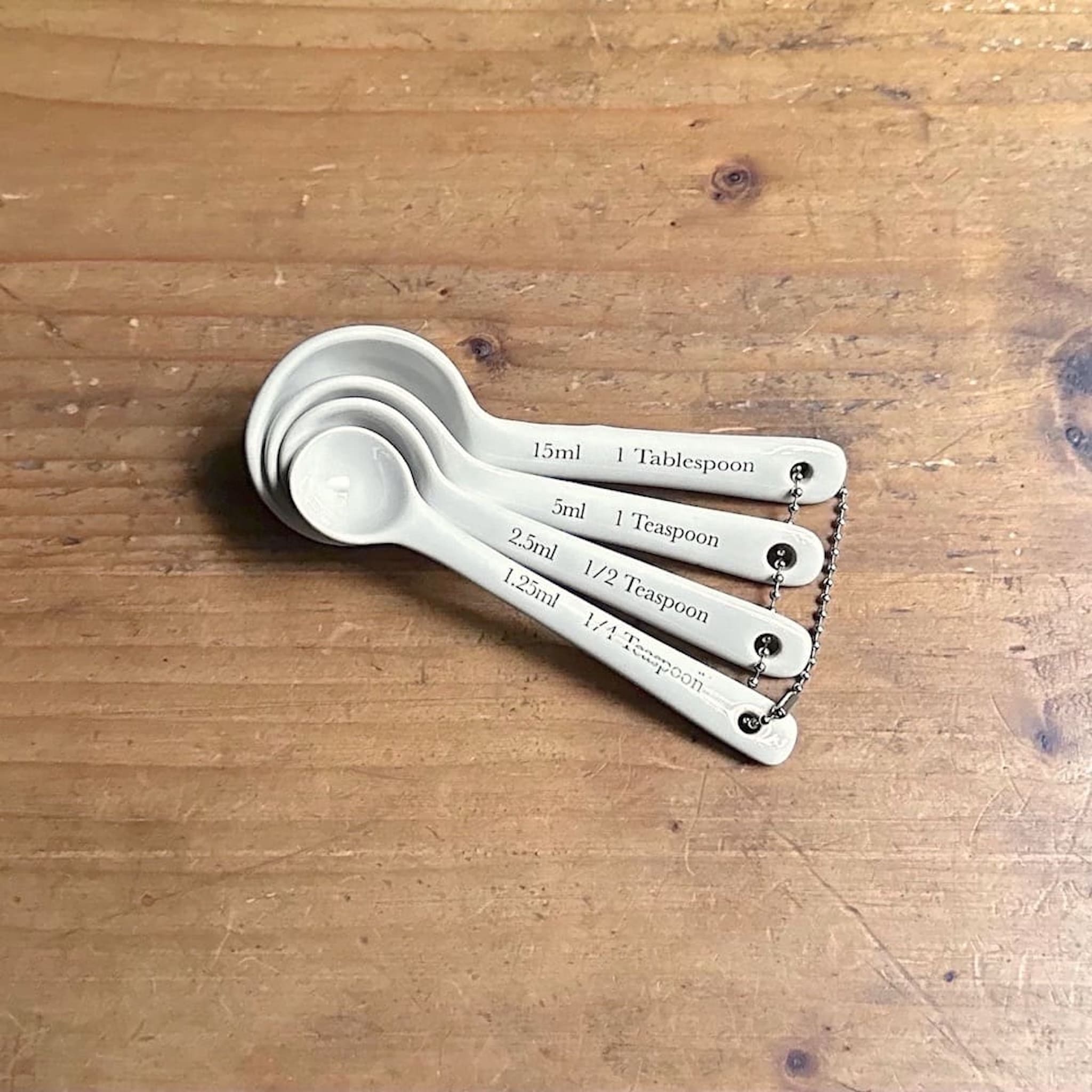Set of four white ceramic measuring spoons on a wooden surface