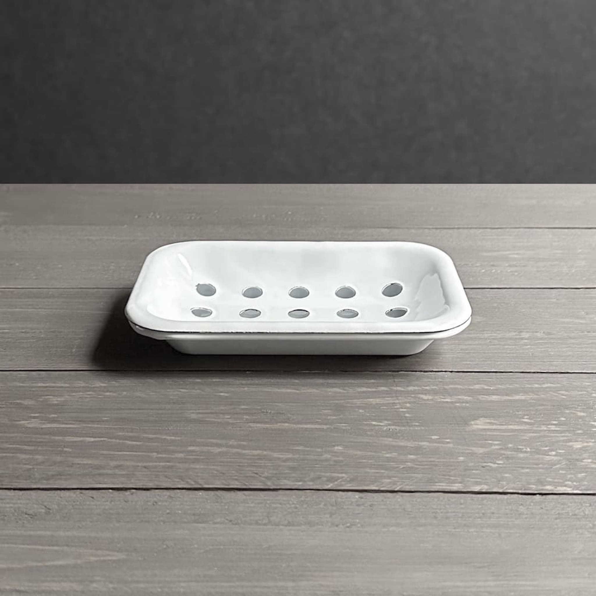 Side view of a white enamel soap dish on a wooden surface with a dark grey background