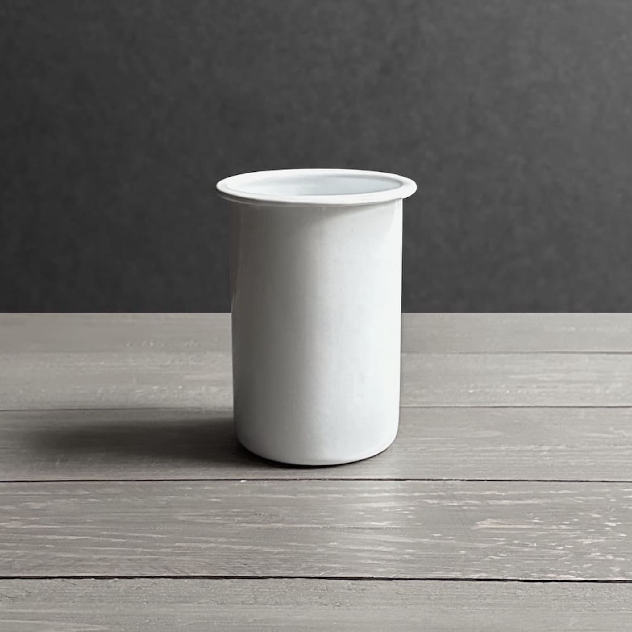 Side view of white enamel toothbrush holder on a wooden surface with a dark grey background