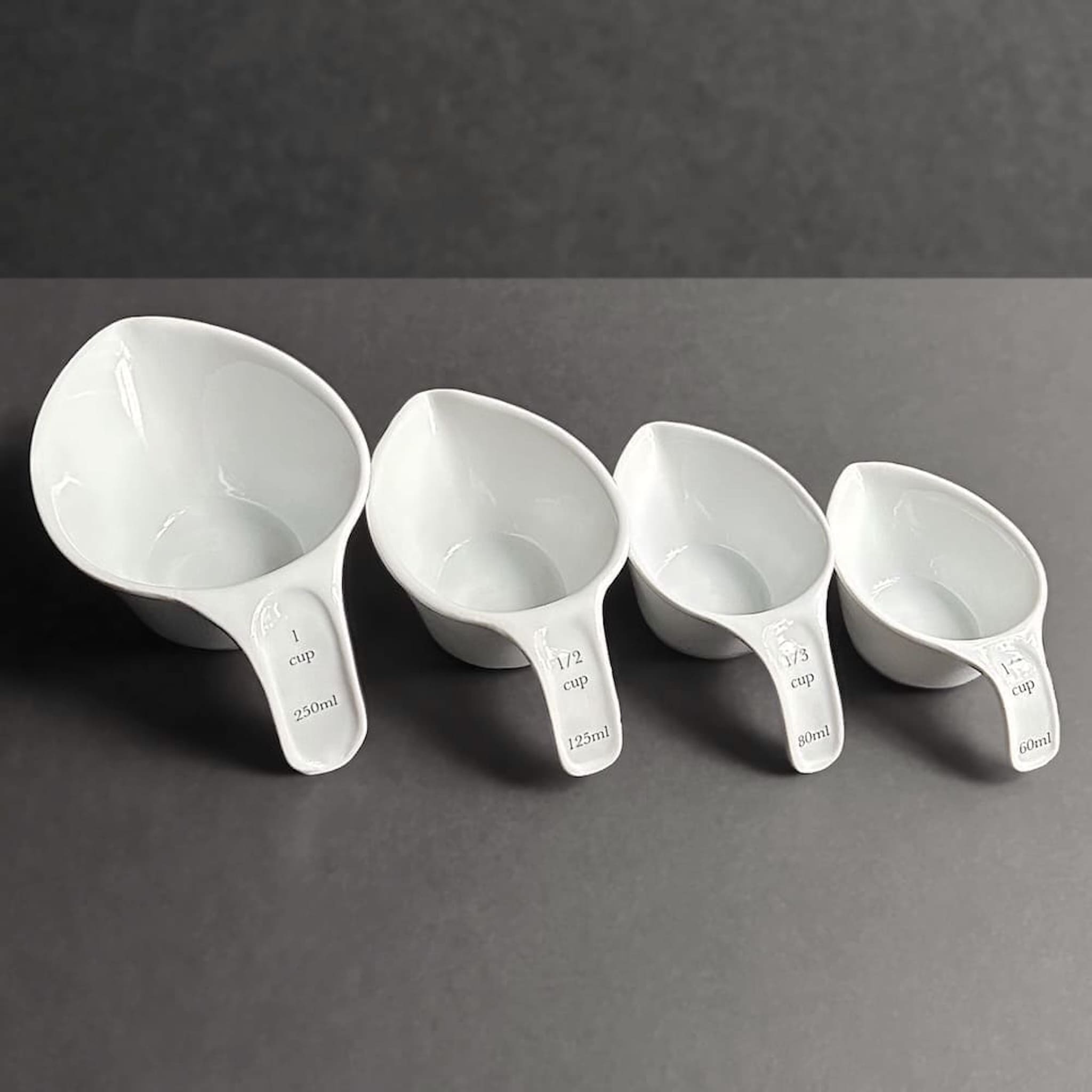 Set of four white measuring cups with measurements on a grey background